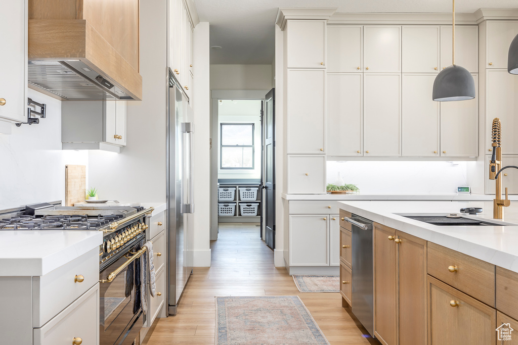 Kitchen with light countertops, light wood-style flooring, wall chimney exhaust hood, and high quality appliances