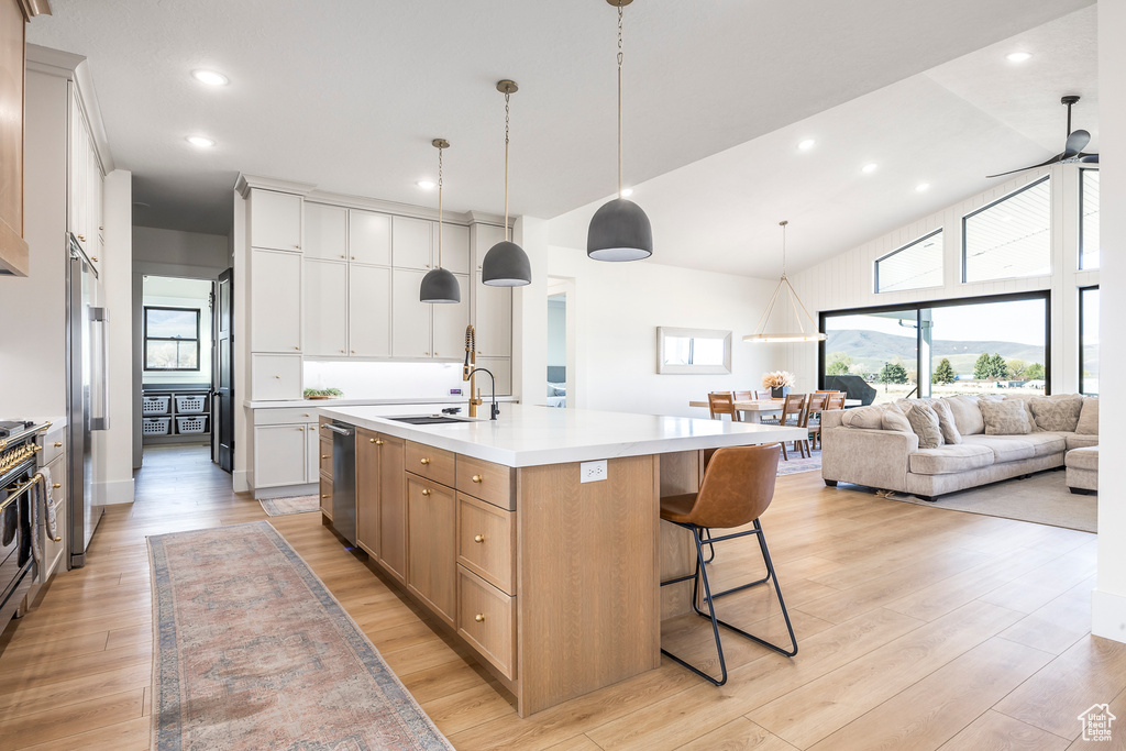 Kitchen featuring light countertops, dishwasher, a sink, a center island with sink, and a breakfast bar area
