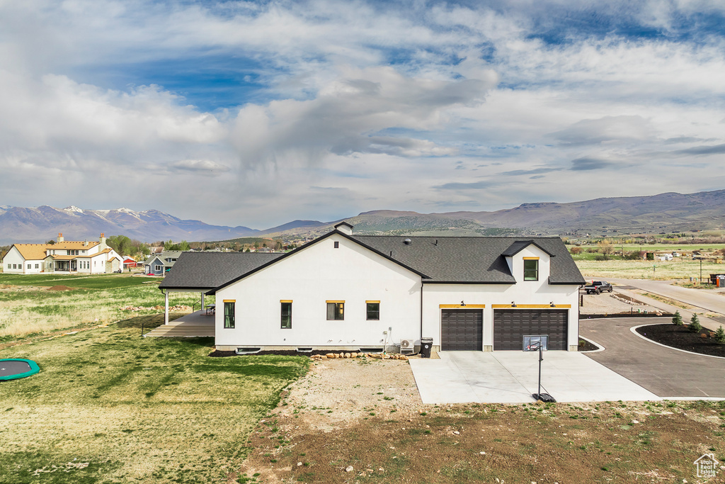View of side of property with an attached garage, a shingled roof, concrete driveway, and a mountain view