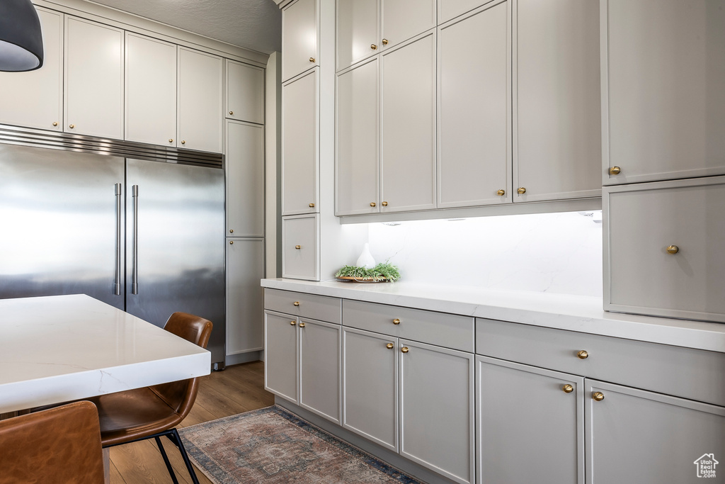 Kitchen featuring stainless steel built in refrigerator, gray cabinetry, dark wood-type flooring, and light stone countertops
