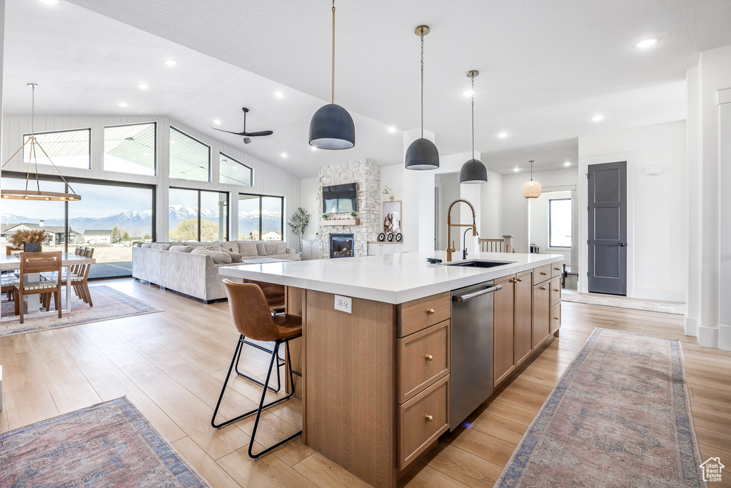 Kitchen with stainless steel dishwasher, a stone fireplace, a sink, brown cabinets, and light countertops