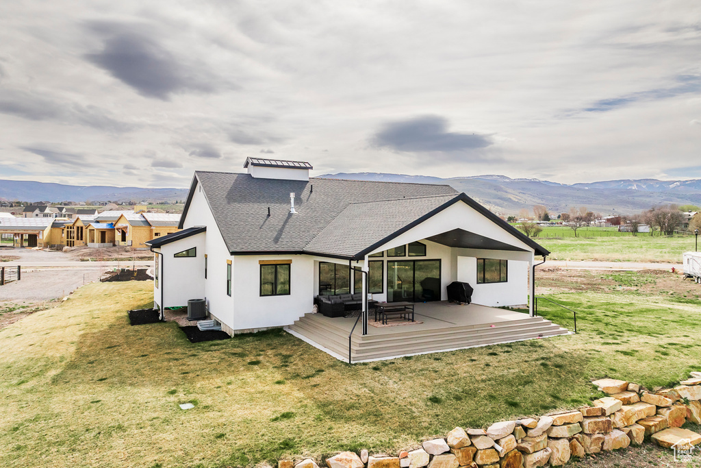 Back of house featuring a deck with mountain view, roof with shingles, central AC unit, a yard, and stucco siding