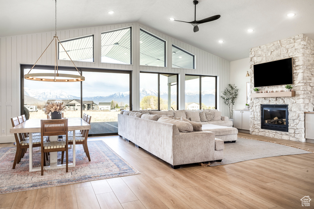 Living room featuring light wood-style flooring, a stone fireplace, high vaulted ceiling, and ceiling fan