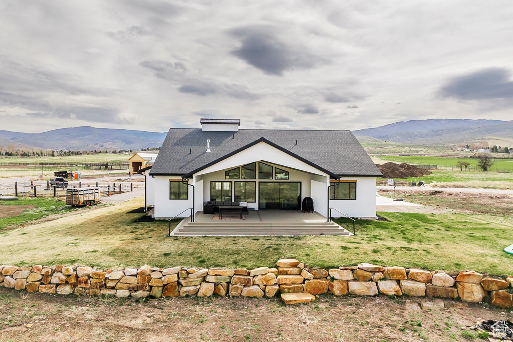 Rear view of house featuring a deck with mountain view, a rural view, a yard, stucco siding, and roof with shingles