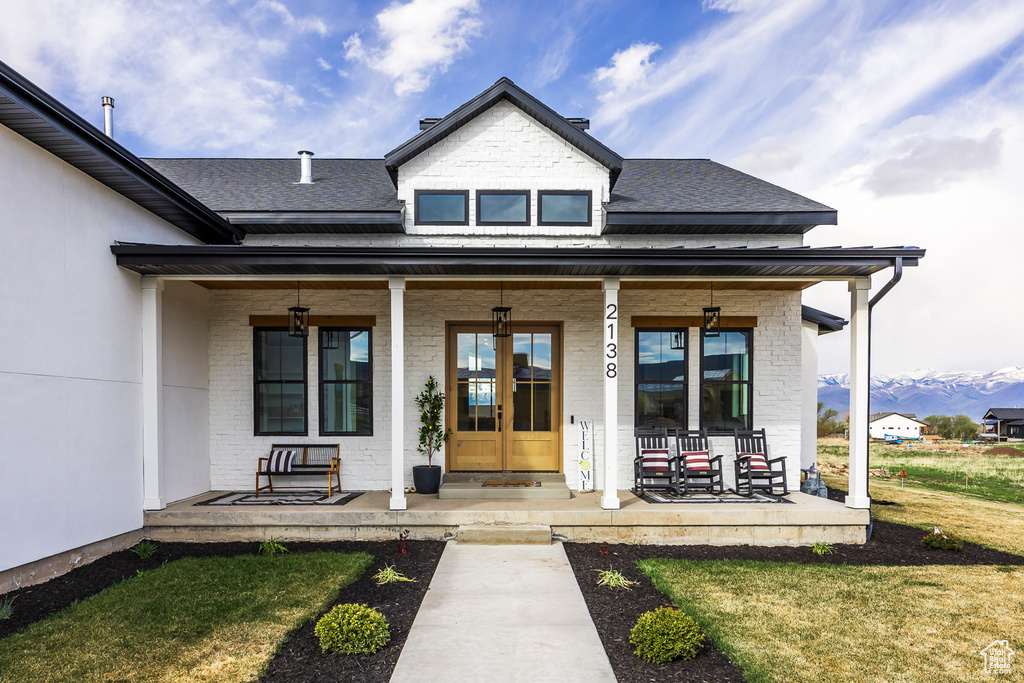 View of exterior entry with brick siding, roof with shingles, a porch, and a yard