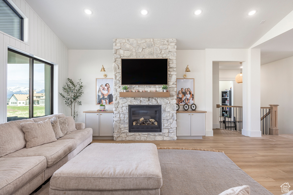 Living room with light wood-type flooring, baseboards, a stone fireplace, and recessed lighting