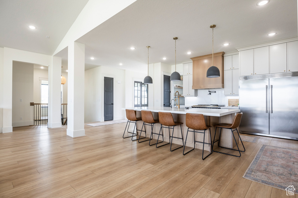 Kitchen featuring a large island with sink, a breakfast bar, light wood-type flooring, light countertops, and appliances with stainless steel finishes