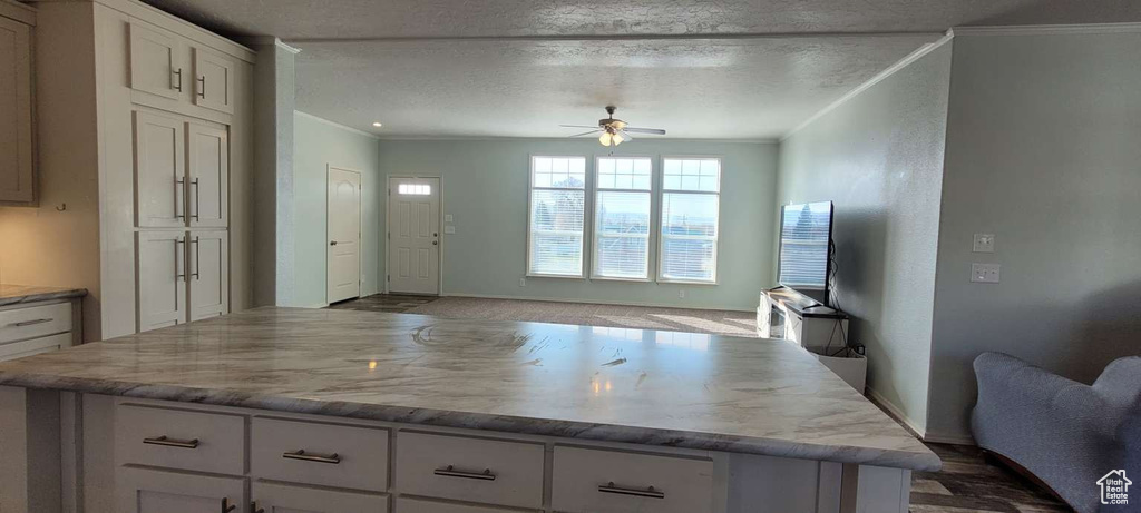 Kitchen with ceiling fan, ornamental molding, white cabinetry, a kitchen island, and baseboards