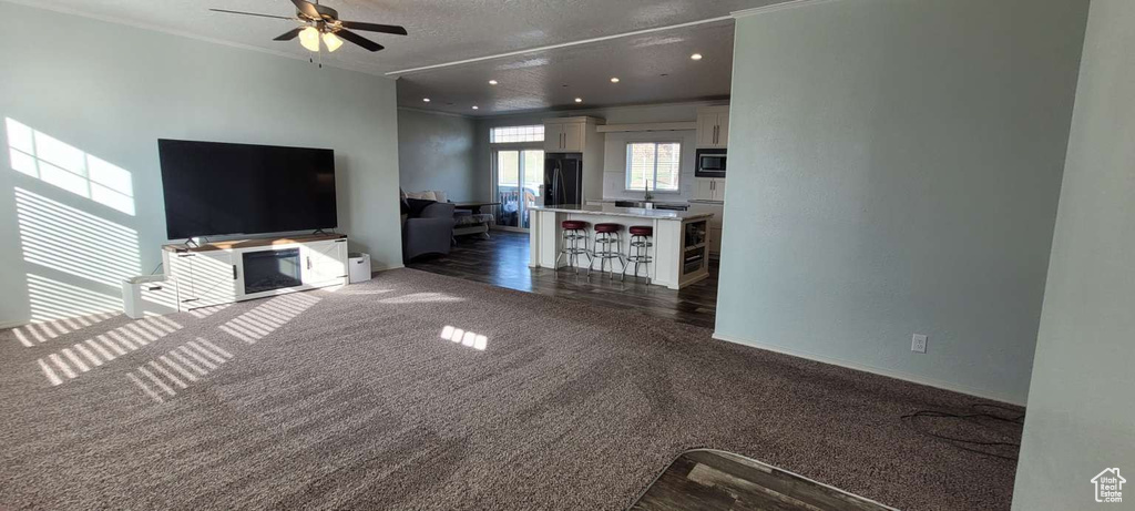 Unfurnished living room with dark carpet, ceiling fan, baseboards, recessed lighting, and a textured ceiling
