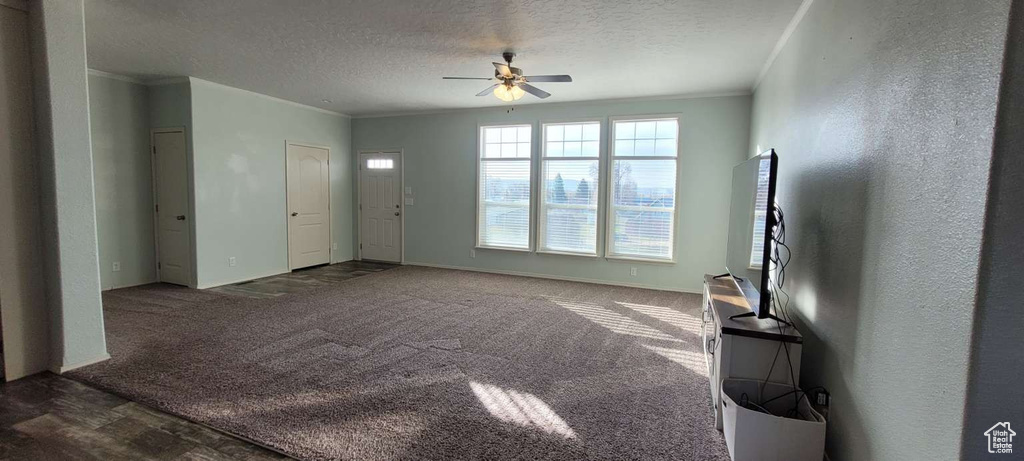 Unfurnished living room featuring ceiling fan, a textured ceiling, ornamental molding, carpet, and baseboards
