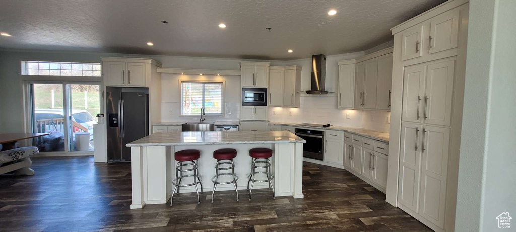 Kitchen with stainless steel appliances, wall chimney exhaust hood, white cabinetry, recessed lighting, and a textured ceiling