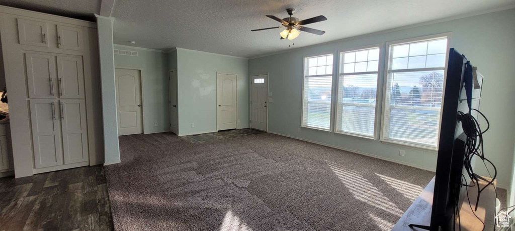 Unfurnished living room with healthy amount of natural light, a ceiling fan, a textured ceiling, baseboards, and crown molding