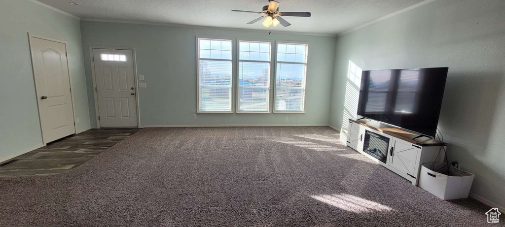 Unfurnished living room featuring crown molding, a ceiling fan, carpet flooring, healthy amount of natural light, and baseboards