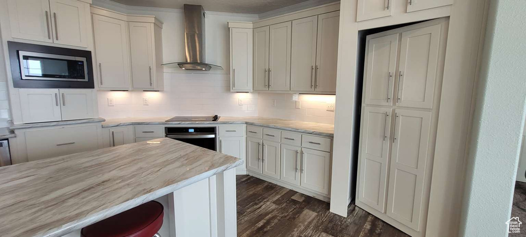 Kitchen with wall oven, stainless steel microwave, wall chimney exhaust hood, dark wood-style flooring, and tasteful backsplash