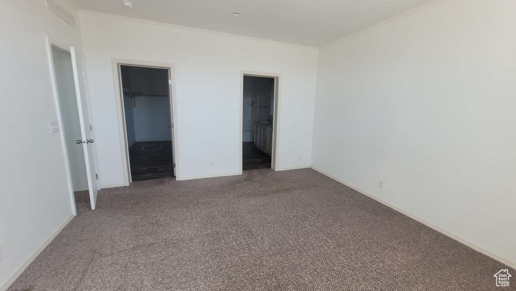 Unfurnished bedroom featuring carpet, a walk in closet, baseboards, and ensuite bath