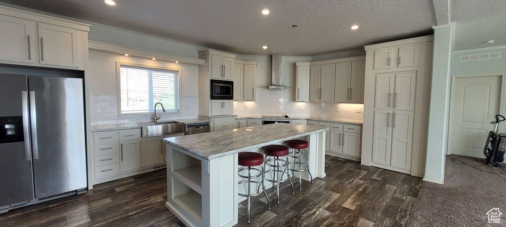 Kitchen featuring stainless steel appliances, wall chimney exhaust hood, a center island, a kitchen breakfast bar, and a sink