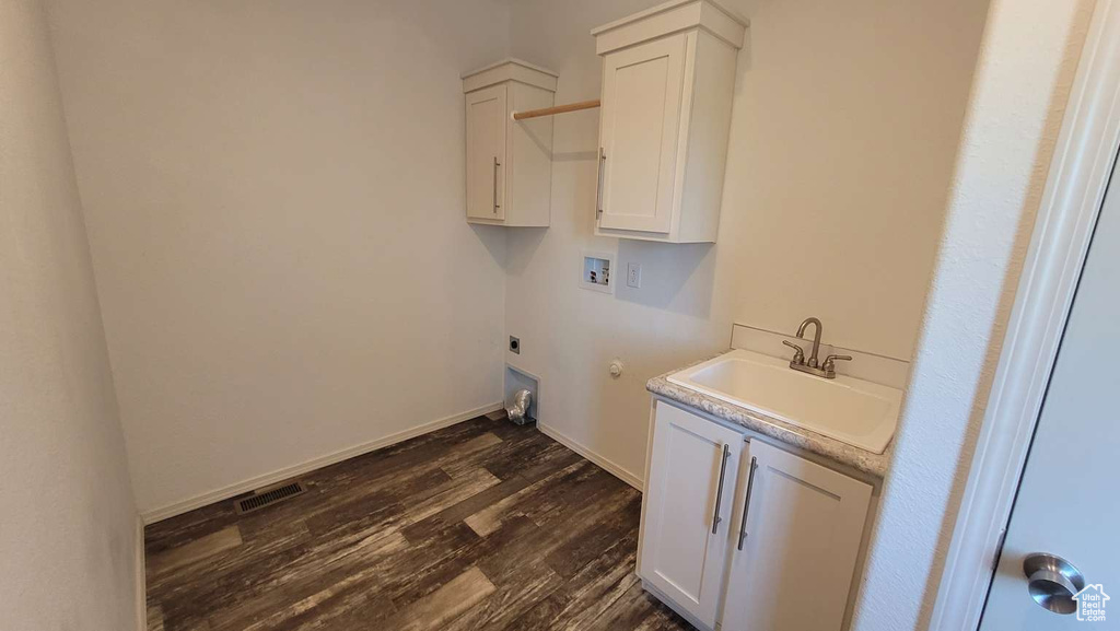 Laundry area with electric dryer hookup, hookup for a washing machine, dark wood finished floors, cabinet space, and baseboards