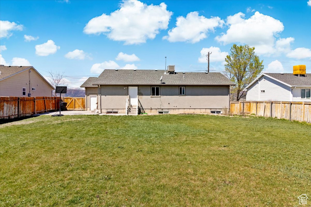 Rear view of house with a fenced backyard, entry steps, and a yard