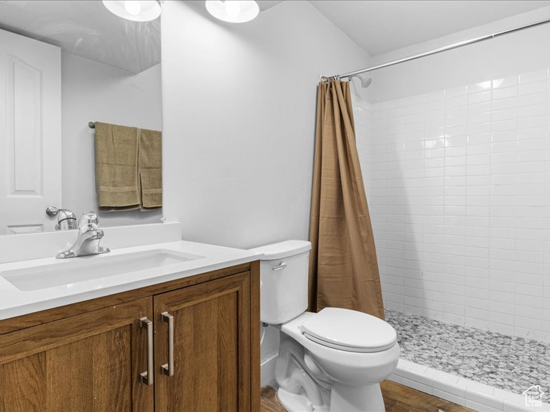 Full bathroom featuring wood finished floors, a tile shower, vanity, and toilet