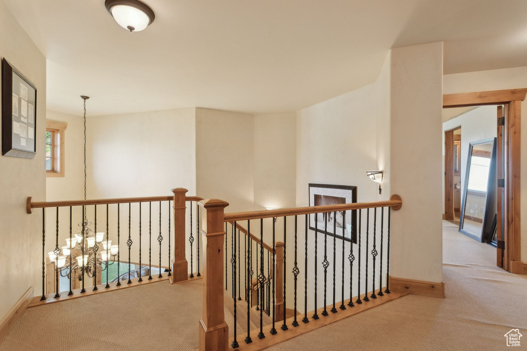 Hall with carpet, an upstairs landing, baseboards, and a chandelier