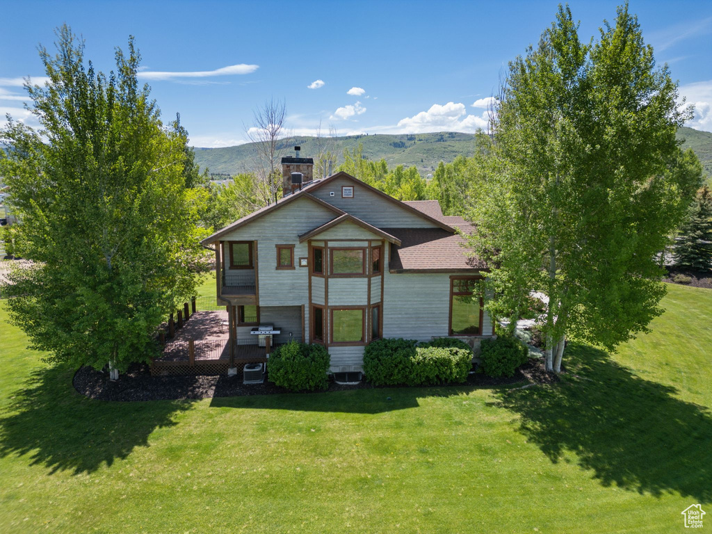 View of front facade with a chimney, a front lawn, central AC unit, and a deck with mountain view