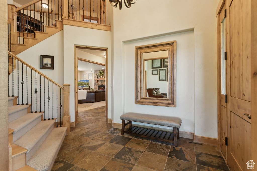 Entryway with baseboards, stone tile floors, stairs, a towering ceiling, and a stone fireplace