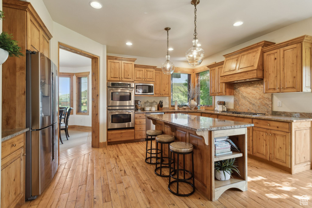 Kitchen featuring stainless steel appliances, open shelves, a breakfast bar, light wood finished floors, and recessed lighting
