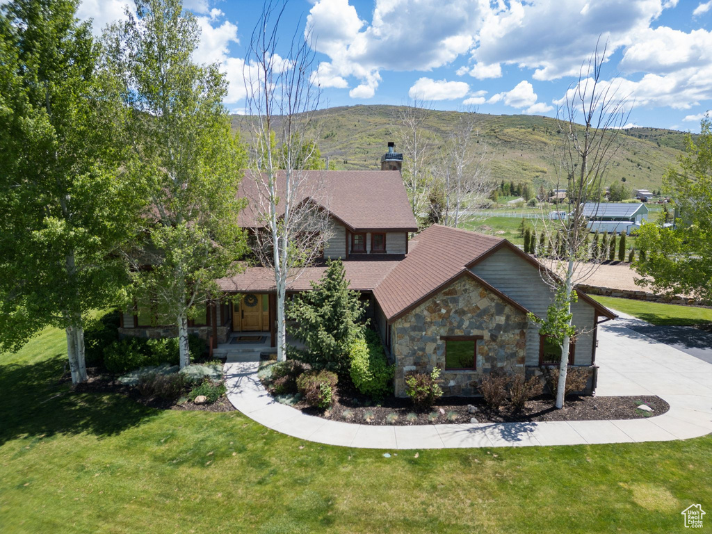 View of front facade featuring stone siding, a chimney, a front yard, and a mountain view