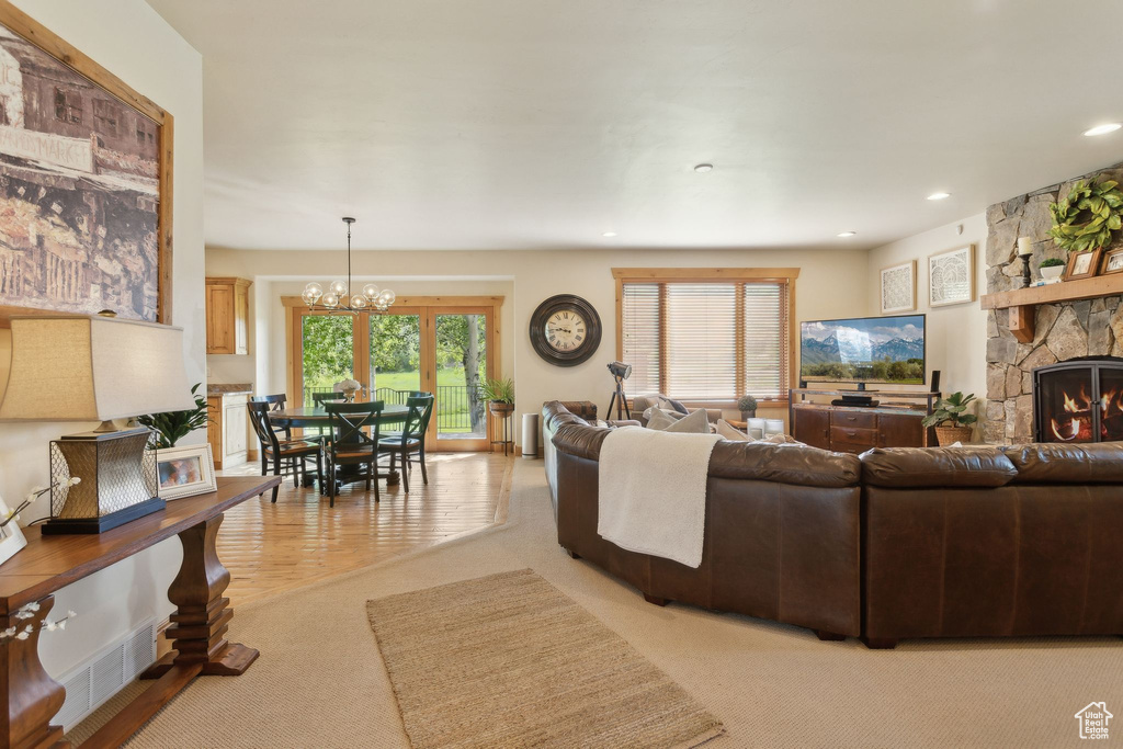 Living area featuring light colored carpet, a chandelier, a stone fireplace, and recessed lighting