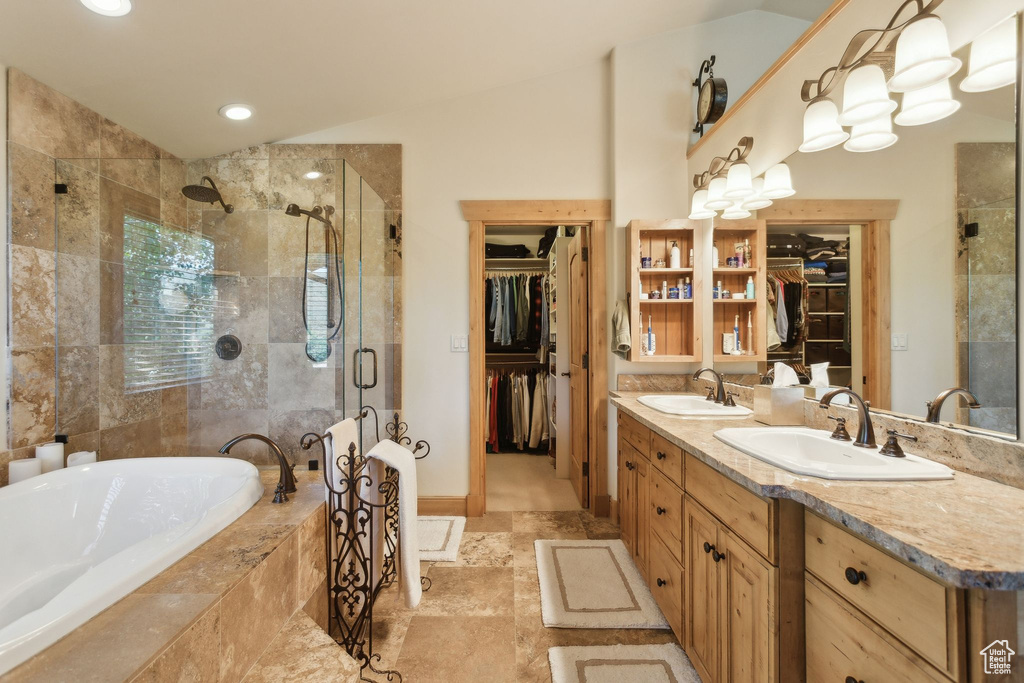 Bathroom featuring a stall shower, a walk in closet, double vanity, a bath, and vaulted ceiling