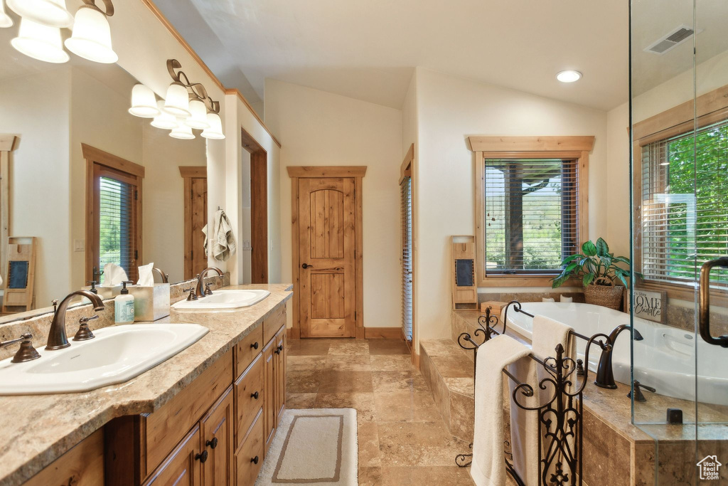 Bathroom featuring double vanity, a bath, vaulted ceiling, and stone finish floors