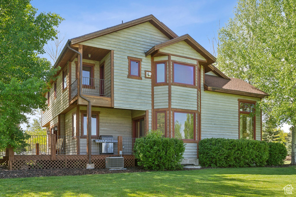 Rear view of property with a balcony, central AC unit, and a lawn