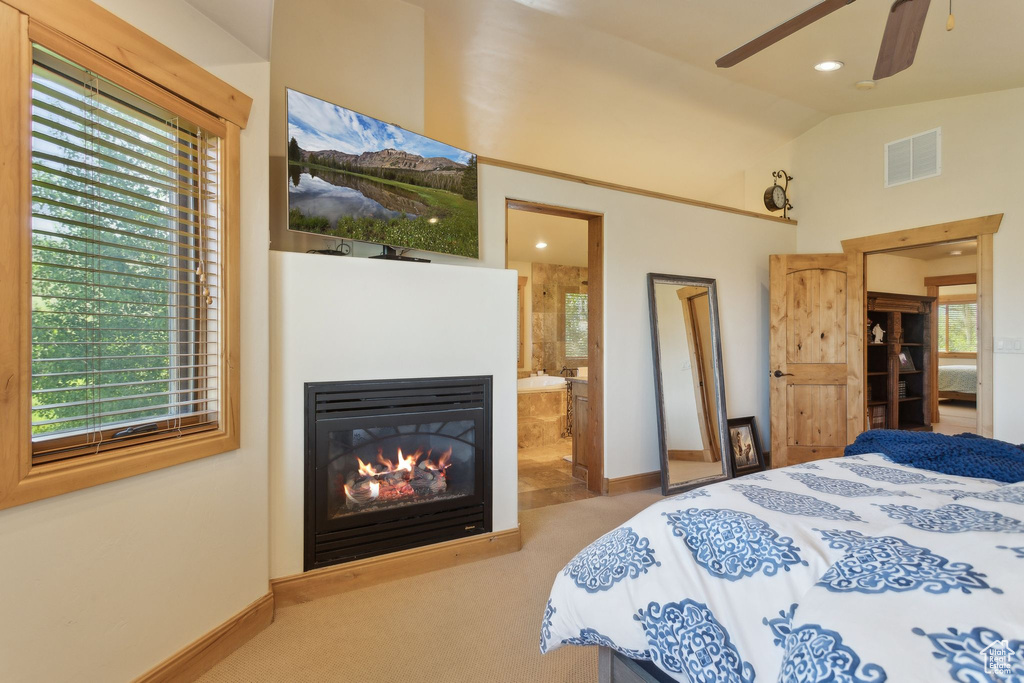 Carpeted bedroom featuring baseboards, vaulted ceiling, multiple windows, connected bathroom, and a glass covered fireplace
