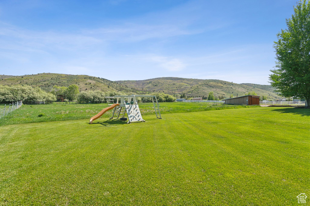 View of grassy yard featuring a playground, a mountain view, and an outdoor structure
