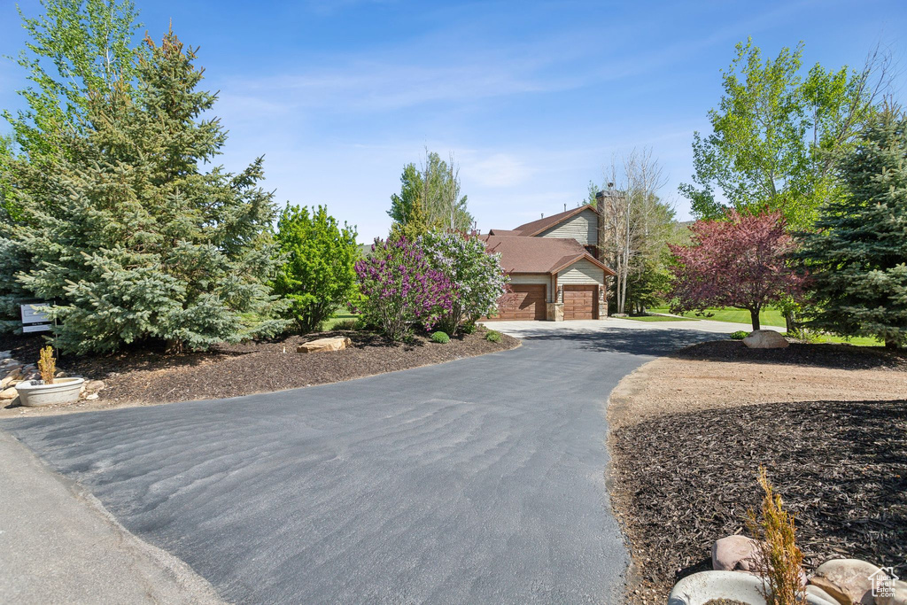 View of property hidden behind natural elements with driveway, brick siding, and an attached garage