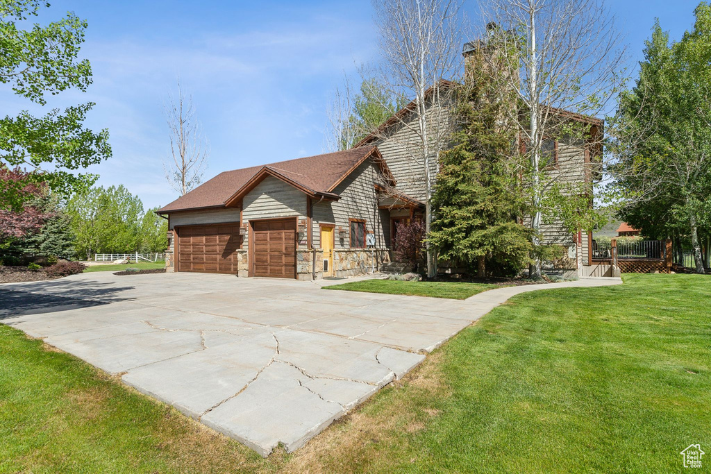 View of front of property featuring a front yard, a garage, driveway, a chimney, and stone siding
