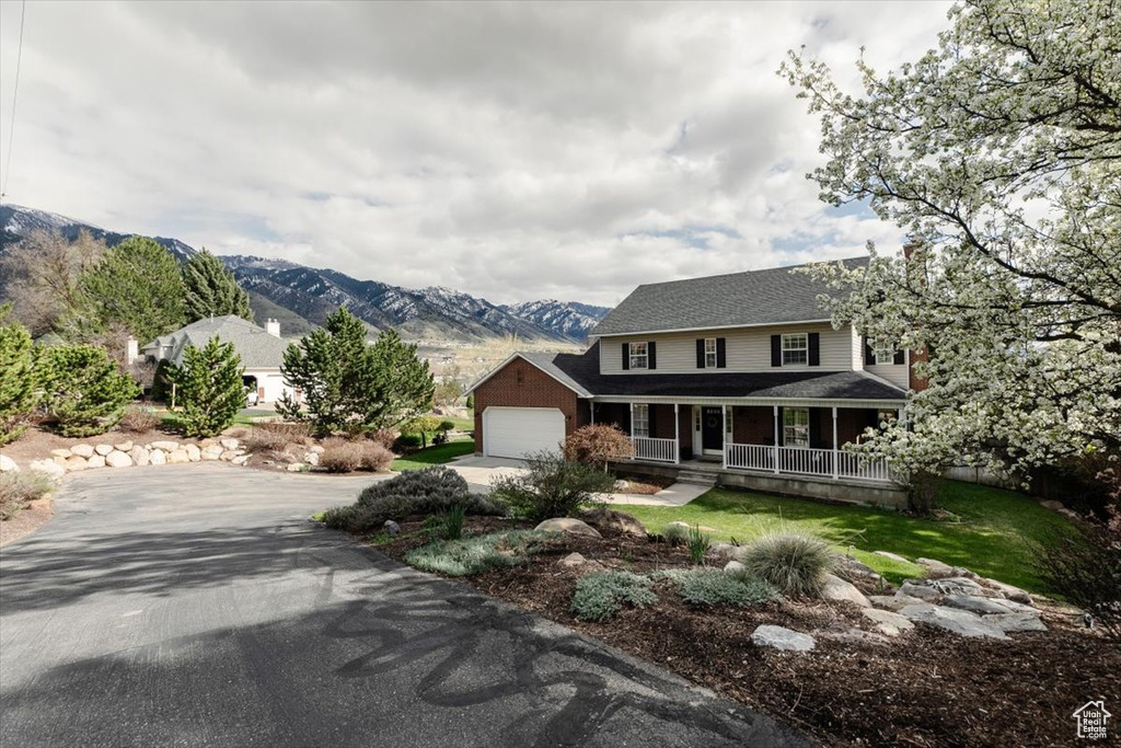 Farmhouse featuring a mountain view, a porch, concrete driveway, an attached garage, and a shingled roof