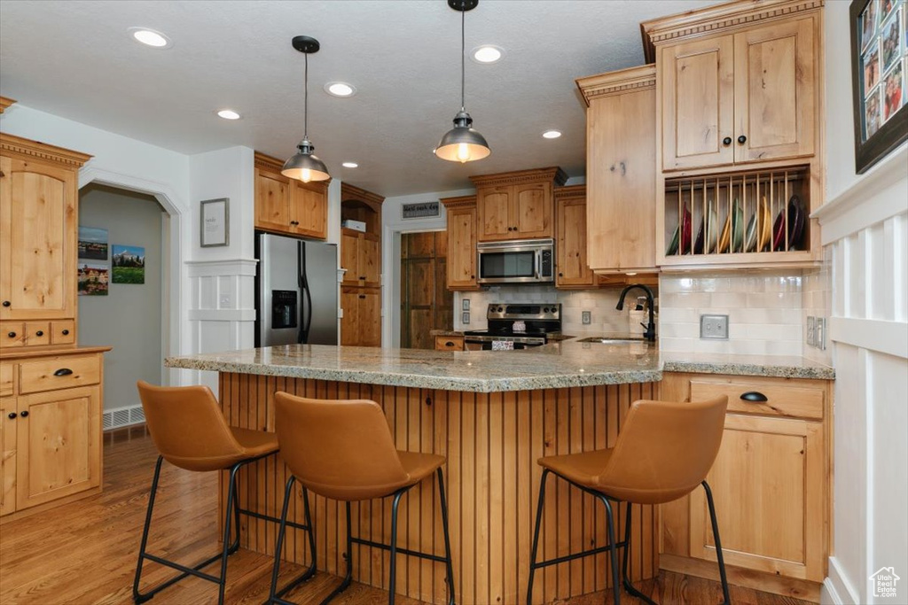 Kitchen with a peninsula, light wood-style flooring, a sink, backsplash, and appliances with stainless steel finishes