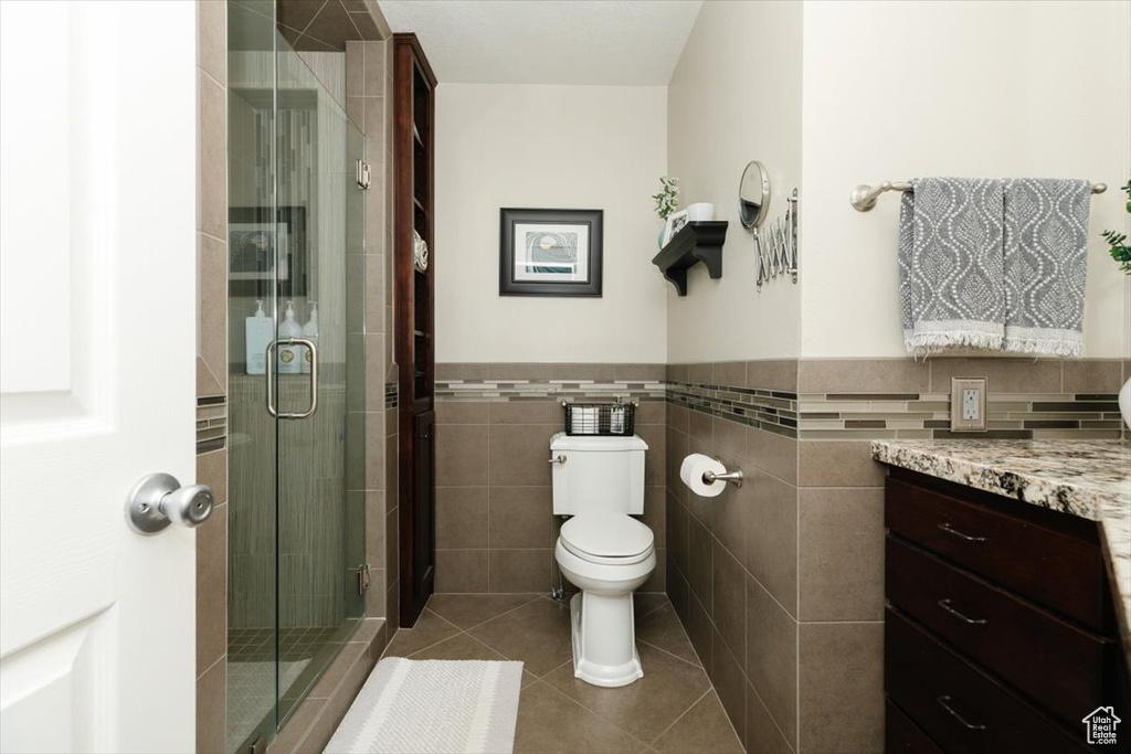 Bathroom featuring tile walls, toilet, a stall shower, and tile patterned floors