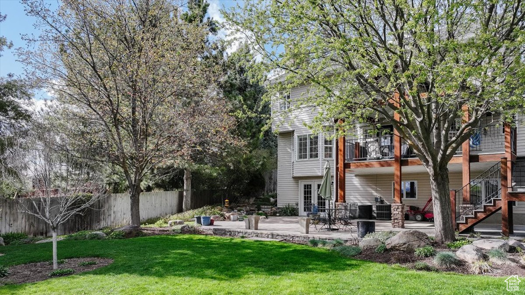 Rear view of property featuring a patio area, a balcony, fence, a yard, and stairs