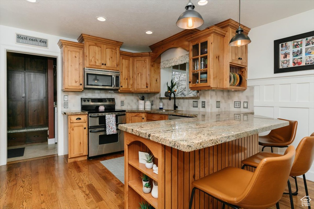 Kitchen featuring a peninsula, a sink, glass insert cabinets, open shelves, and appliances with stainless steel finishes