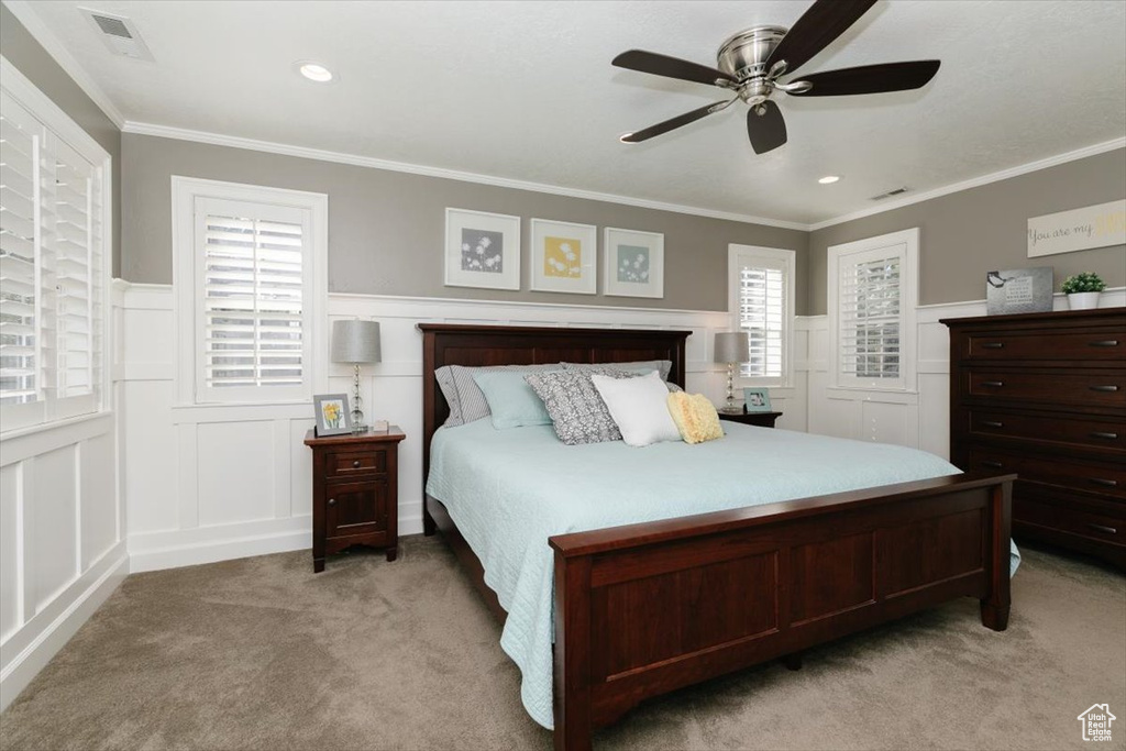 Bedroom with a wainscoted wall, light colored carpet, a ceiling fan, a decorative wall, and ornamental molding
