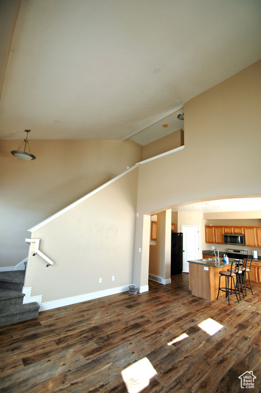 Unfurnished living room with a sink, high vaulted ceiling, stairs, baseboards, and dark wood-style floors