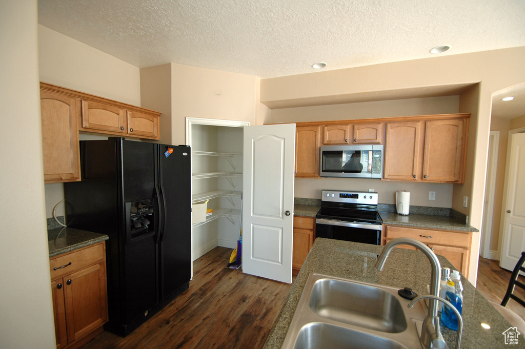 Kitchen featuring a textured ceiling, appliances with stainless steel finishes, dark countertops, a sink, and dark wood-type flooring