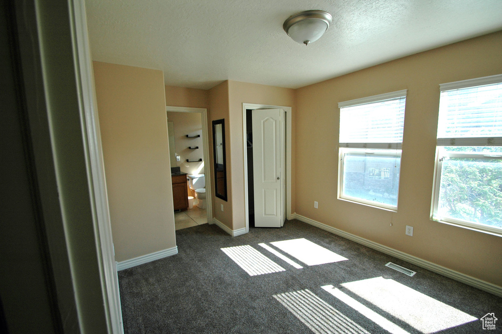 Unfurnished bedroom featuring baseboards, dark carpet, a textured ceiling, and visible vents