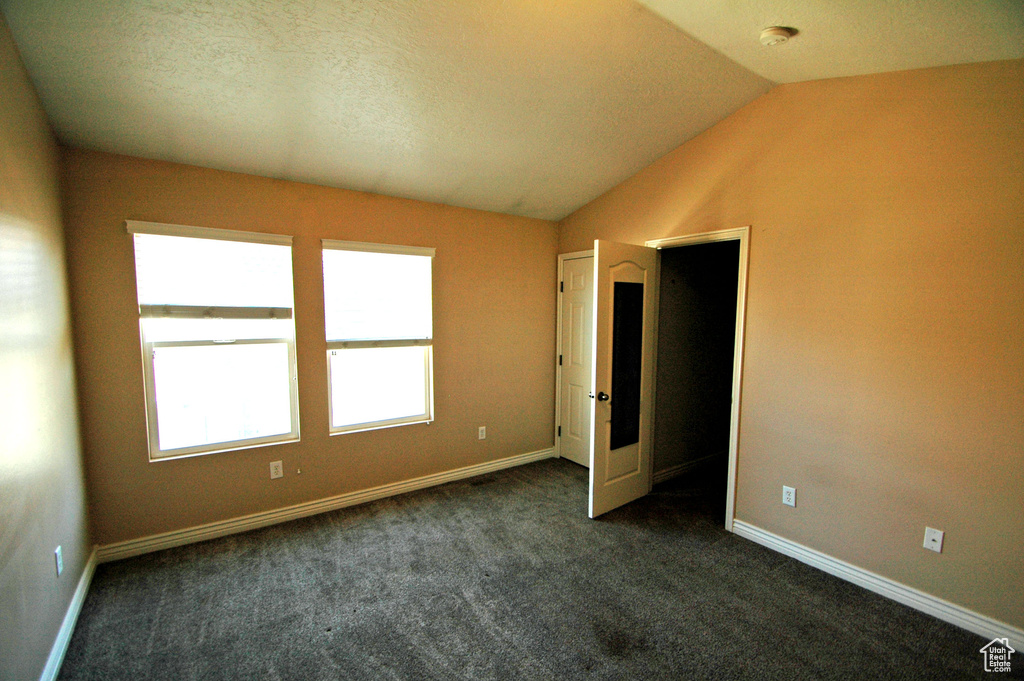 Spare room with dark carpet, baseboards, and lofted ceiling