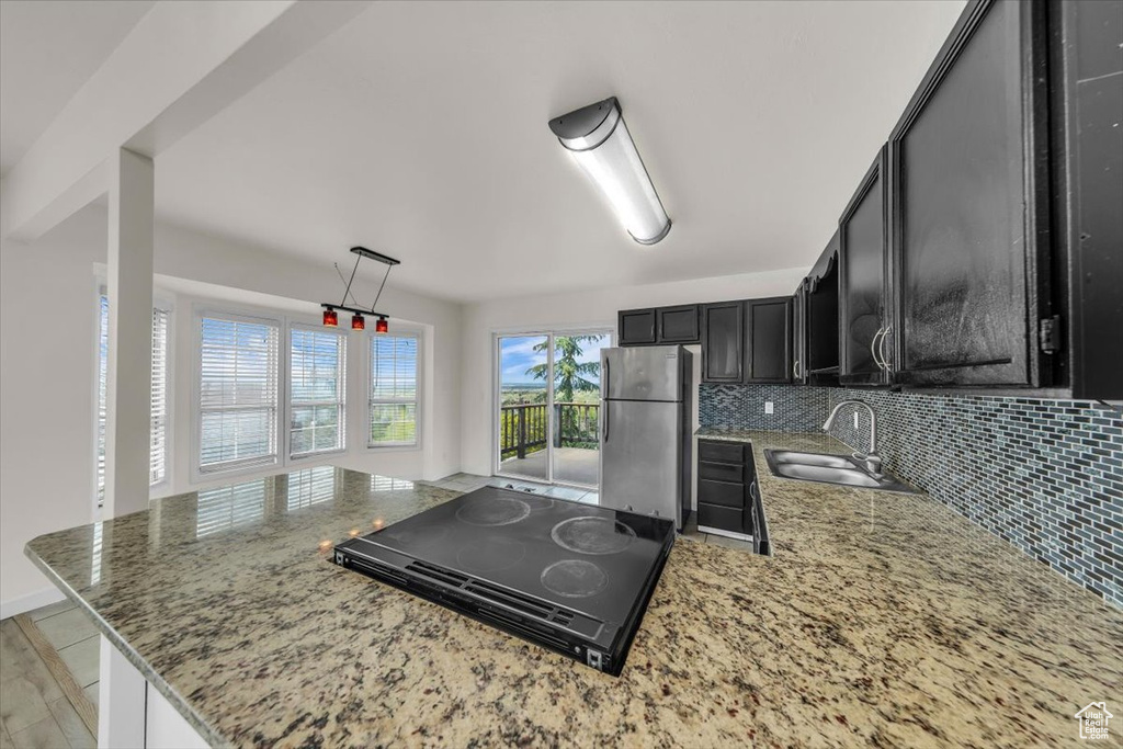 Kitchen with a sink, freestanding refrigerator, light stone counters, dark cabinets, and cooktop