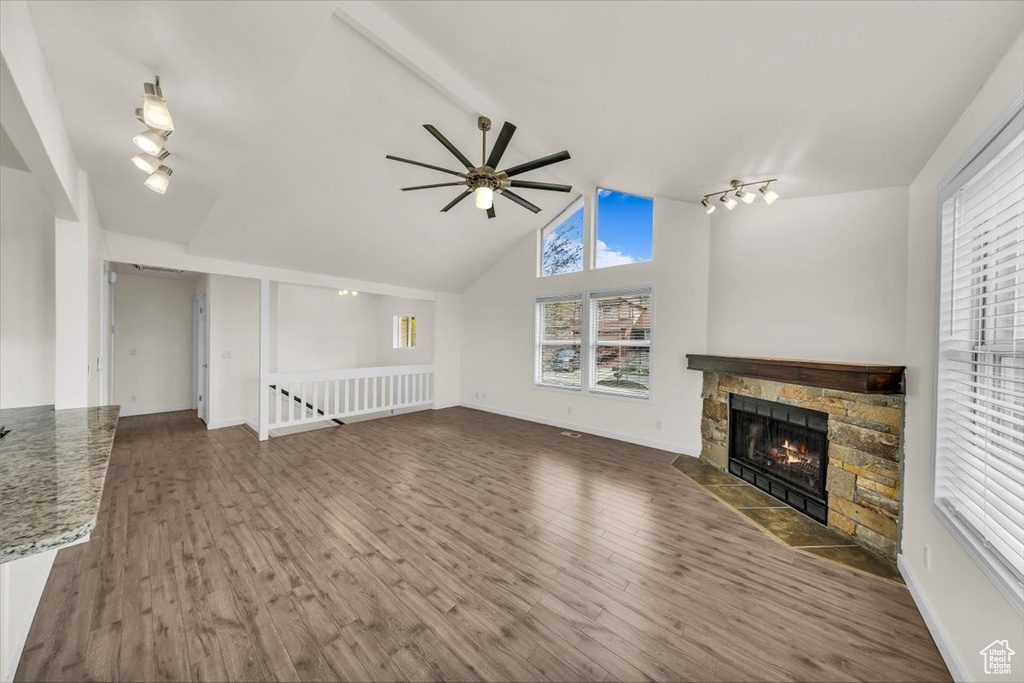 Unfurnished living room with a ceiling fan, wood finished floors, a stone fireplace, rail lighting, and baseboards
