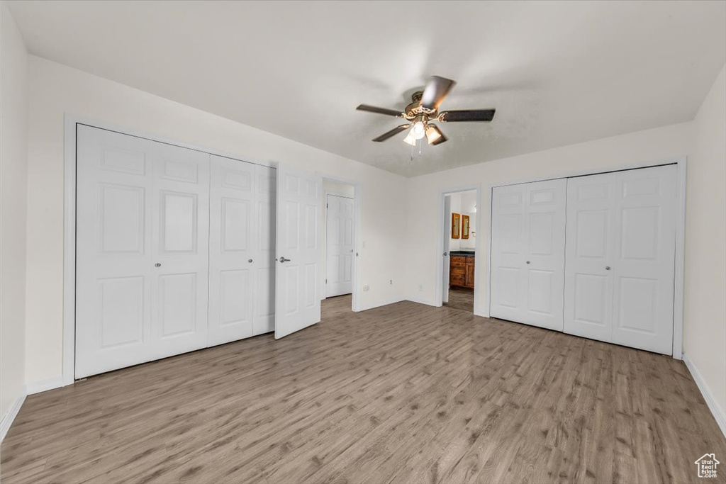 Unfurnished bedroom with light wood finished floors, baseboards, a ceiling fan, multiple closets, and ensuite bath