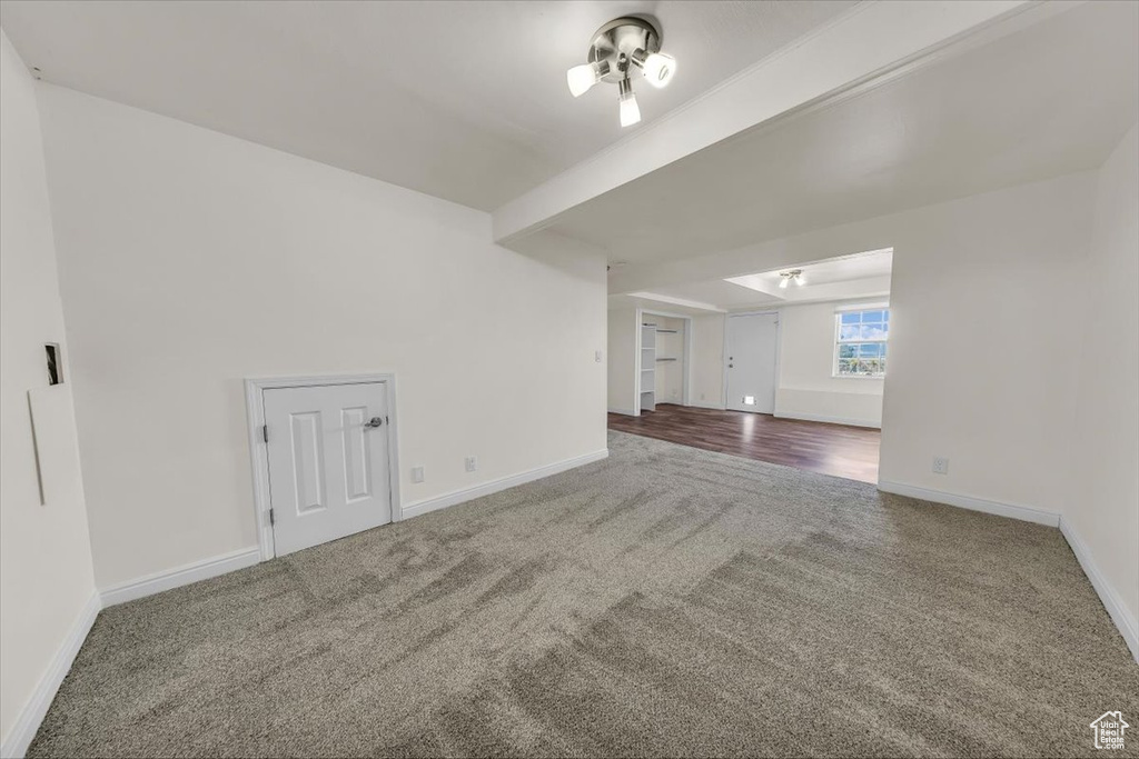Carpeted spare room featuring baseboards and beamed ceiling